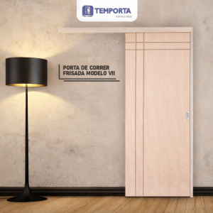 Porta de correr frisada modelo VII em madeira clara instalada em ambiente interno moderno, com acabamento elegante e trilho superior aparente, acompanhada de abajur preto com iluminação suave, ideal para otimização de espaços e decoração contemporânea.