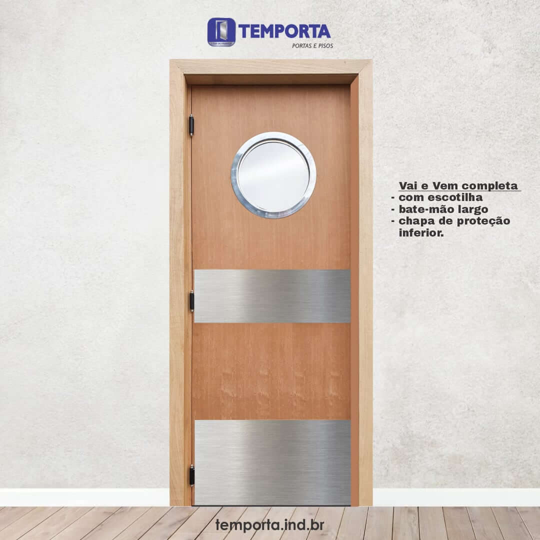 Porta vai e vem de madeira com visor redondo tipo escotilha, chapa de proteção em aço inox e bate-mão largo. A porta está instalada em batente de madeira clara, sobre piso amadeirado, com destaque para as características do produto e logotipo da Temporta ao fundo.